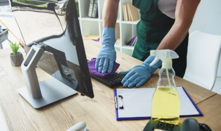 Person cleaning a computer keyboard with gloves and a cloth on a desk, symbolizing digital spring cleaning and keeping personal information up to date.