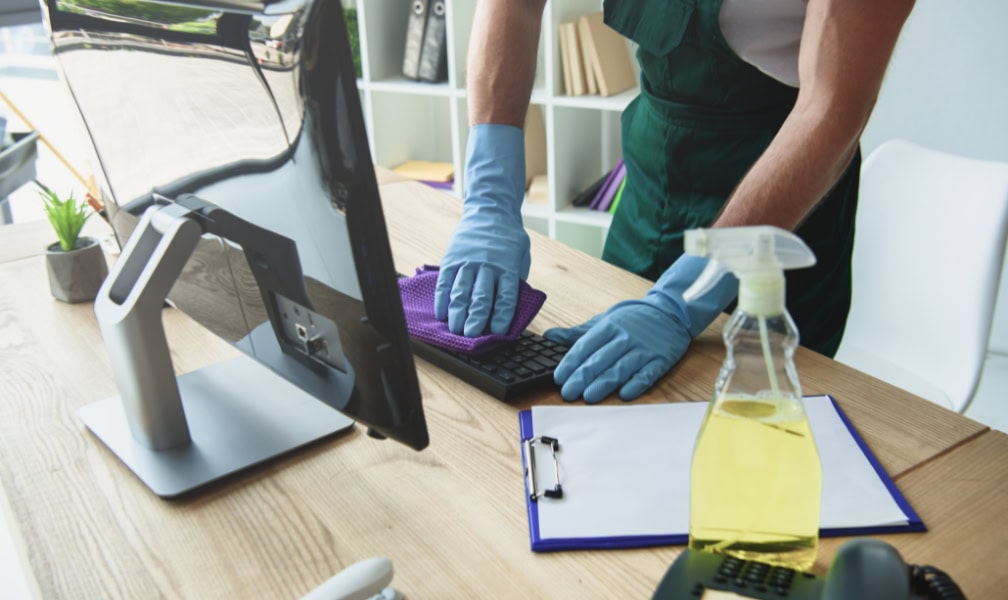 Person cleaning a computer keyboard with gloves and a cloth on a desk, symbolizing digital spring cleaning and keeping personal information up to date.