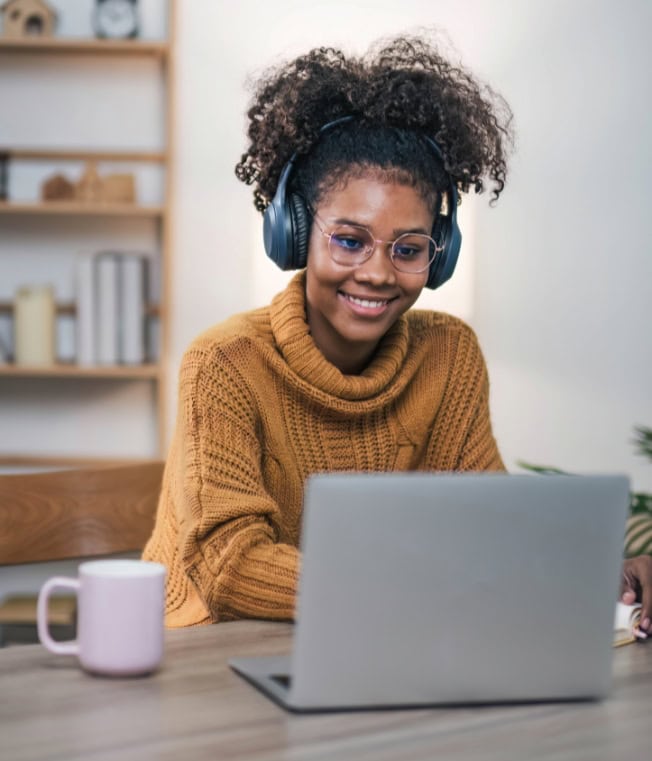 Person wearing headphones and using a laptop in a cozy study space, representing learning about online safety.
